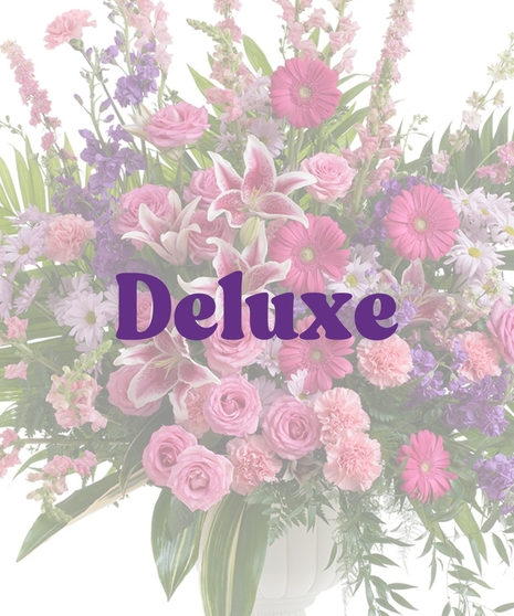 Feminine urn floral arrangement with pink rose lilies, roses, carnations, gerbera daisies, purple stock, and greenery in a white pedestal vase