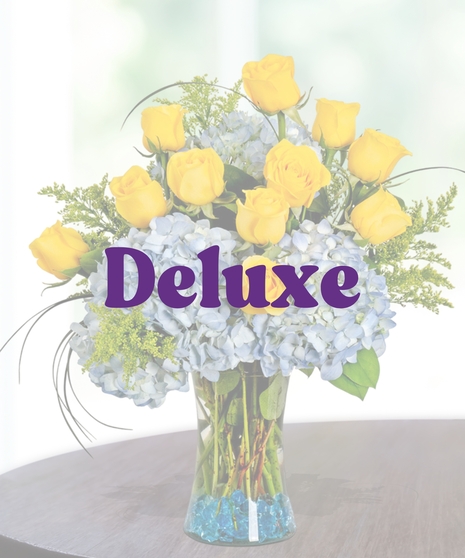 Southern Pride collegiate floral arrangement featuring yellow roses, light blue hydrangeas, golden solidago, and bear grass in a clear glass vase with blue decorative gems.