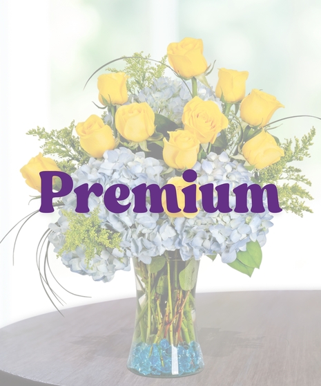 Southern Pride collegiate floral arrangement featuring yellow roses, light blue hydrangeas, golden solidago, and bear grass in a clear glass vase with blue decorative gems.
