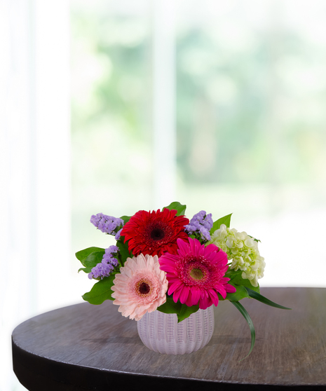 Grateful for You floral arrangement featuring magenta and blush gerbera daisies, pink carnations, and purple statice in a textured lavender glass vase.