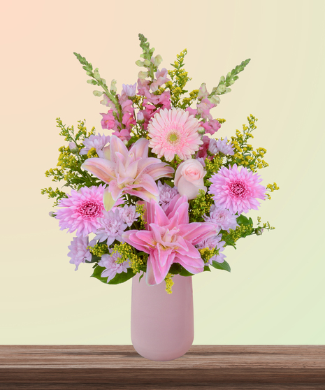 Mother’s Glow flower arrangement with pink lilies, blush roses, gerbera daisies, snapdragons, and hydrangeas in a matte pink vase – a Mother’s Day bouquet.