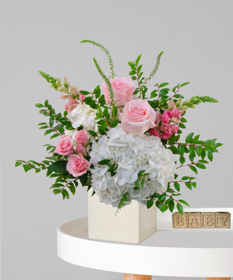 It’s a Girl flower arrangement with pink roses, white hydrangeas, and snapdragons in an ivory cube vase