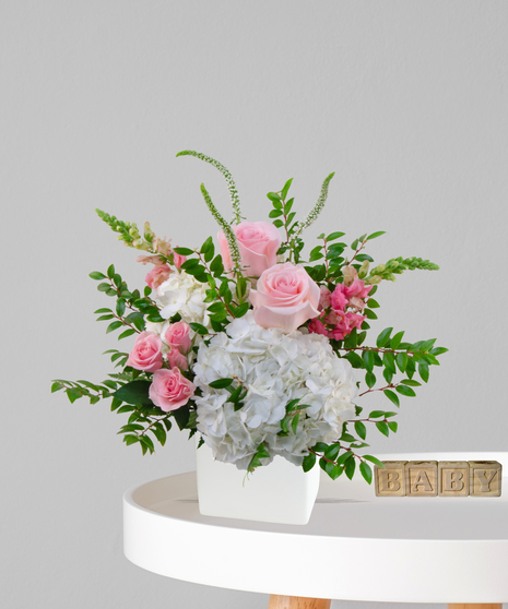 It’s a Girl flower arrangement with pink roses, white hydrangeas, and snapdragons in an ivory cube vase