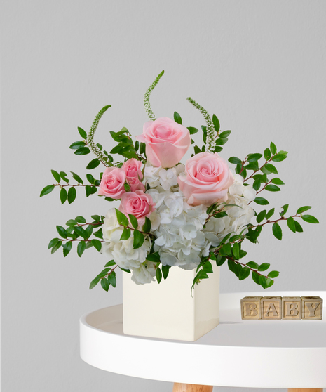 It’s a Girl flower arrangement with pink roses, white hydrangeas, and snapdragons in an ivory cube vase