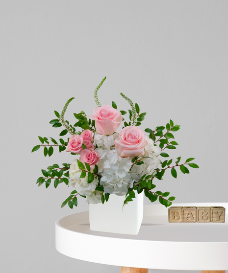 It’s a Girl flower arrangement with pink roses, white hydrangeas, and snapdragons in an ivory cube vase