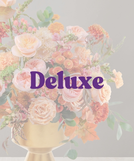 Elegant peach and blush fall flower arrangement with roses, mums, and autumn foliage in a gold pedestal vase