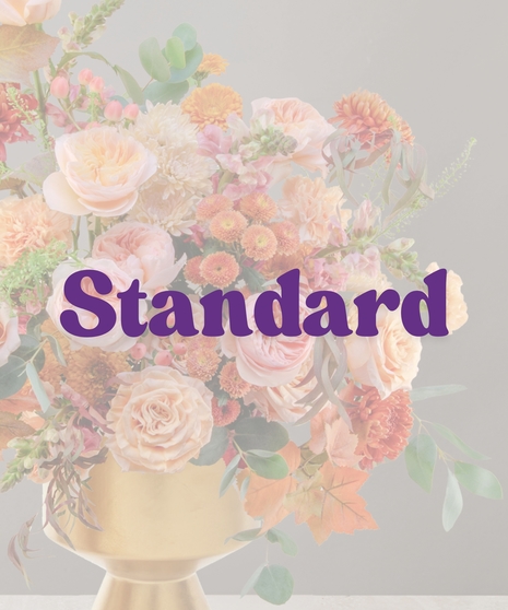 Elegant peach and blush fall flower arrangement with roses, mums, and autumn foliage in a gold pedestal vase