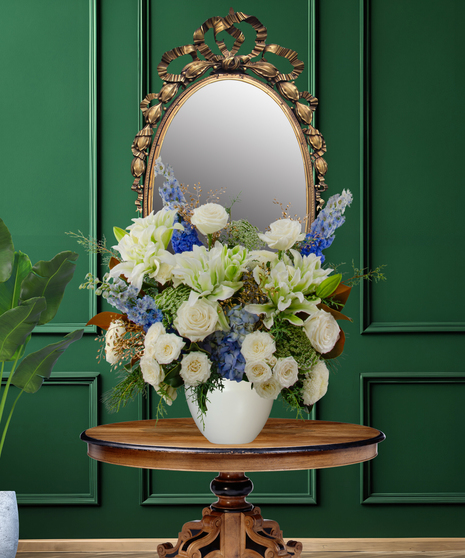 Miracle of Lights Hanukkah flower arrangement with white roses, white lilies, blue delphinium, blue thistle, green spider mums, and magnolia leaves in a white vase