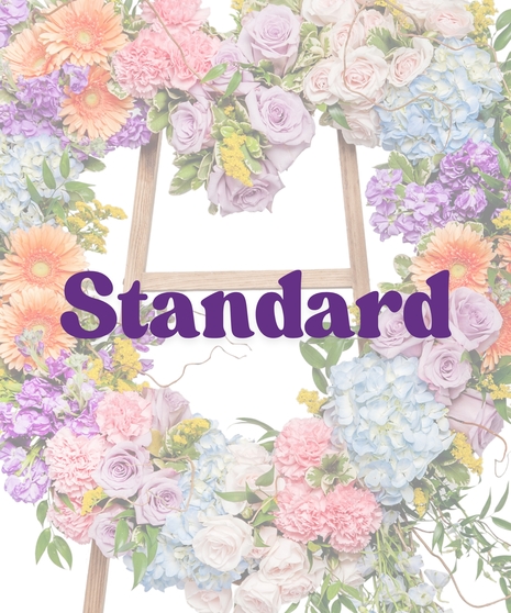 Pastel heart-shaped floral tribute with gerbera daisies, roses, hydrangea, and greenery on a wooden easel from Billy Heroman’s Florist in Baton Rouge