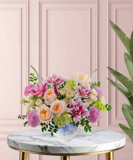 Heart of the Home Mother's Day flower arrangement featuring peach garden roses, pink and white rose lilies, lavender mums, and veronica in a marbled blue and white bowl.