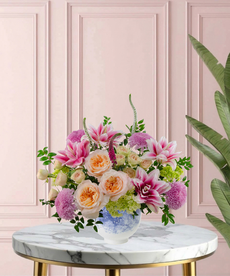 Heart of the Home Mother's Day flower arrangement featuring peach garden roses, pink and white rose lilies, lavender mums, and veronica in a marbled blue and white bowl.