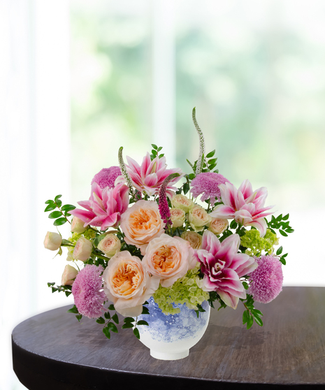 Heart of the Home Mother's Day flower arrangement featuring peach garden roses, pink and white rose lilies, lavender mums, and veronica in a marbled blue and white bowl.