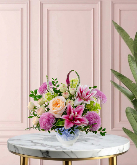 Heart of the Home Mother's Day flower arrangement featuring peach garden roses, pink and white rose lilies, lavender mums, and veronica in a marbled blue and white bowl.