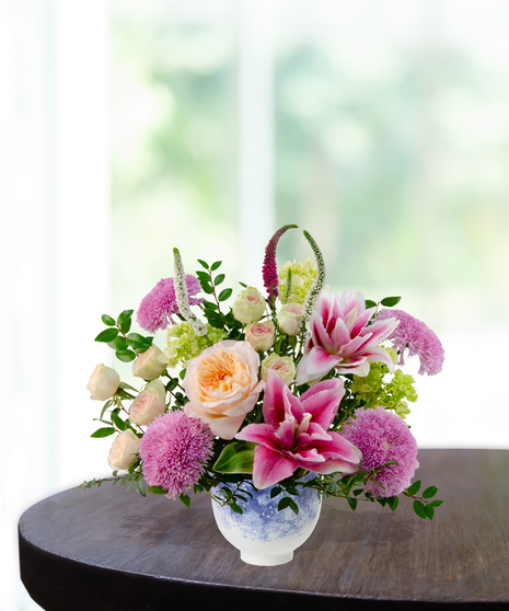 Heart of the Home Mother's Day flower arrangement featuring peach garden roses, pink and white rose lilies, lavender mums, and veronica in a marbled blue and white bowl.