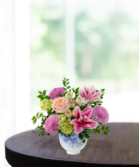 Heart of the Home Mother's Day flower arrangement featuring peach garden roses, pink and white rose lilies, lavender mums, and veronica in a marbled blue and white bowl.
