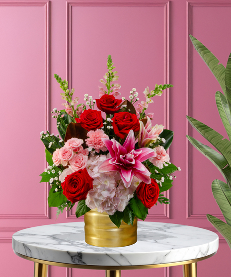 Queen of Hearts exclusive Valentine's flower arrangement with red roses, pink lilies, pink hydrangeas, pink snapdragons, and spray roses in a ribbed gold metallic vase.