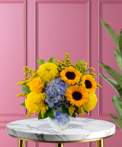 Hello Sunshine exclusive Valentine's Day friendship arrangement with sunflowers, yellow roses, and blue hydrangeas in a blue-and-white marbled vase.