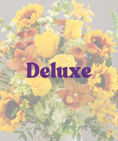 Goldie flower arrangement with yellow roses, sunflowers, cymbidium orchids, and greenery in a ceramic wheat-patterned vase