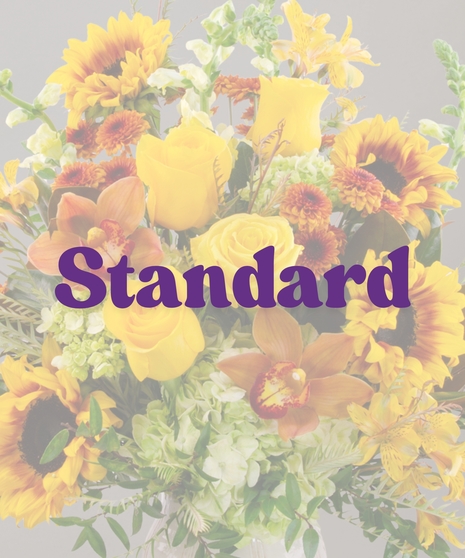 Goldie flower arrangement with yellow roses, sunflowers, cymbidium orchids, and greenery in a ceramic wheat-patterned vase