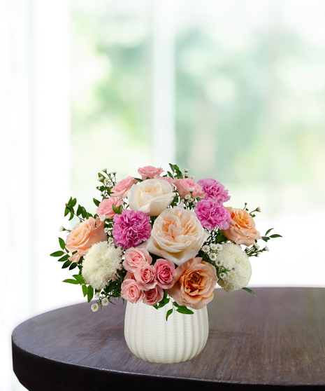 Berry Blush floral arrangement featuring hot pink roses, soft peach roses, pink carnations, white pompon mums, and spray roses in a textured white ceramic vase