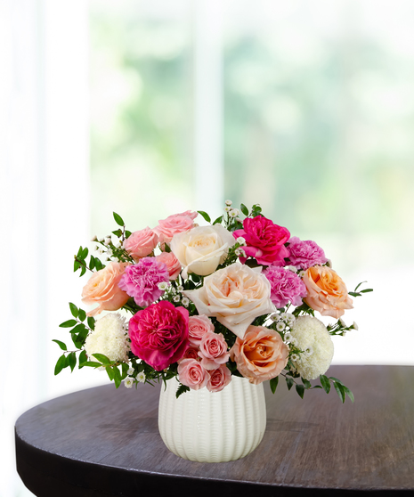 Berry Blush floral arrangement featuring hot pink roses, soft peach roses, pink carnations, white pompon mums, and spray roses in a textured white ceramic vase