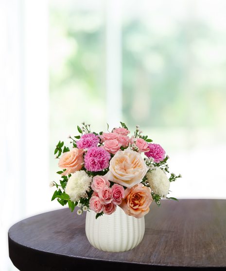 Berry Blush floral arrangement featuring hot pink roses, soft peach roses, pink carnations, white pompon mums, and spray roses in a textured white ceramic vase