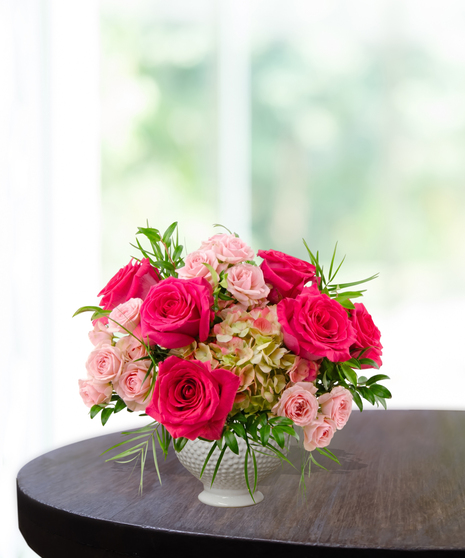 Tickled Pink everyday floral arrangement featuring hot pink roses, light pink spray roses, and lime-green hydrangeas in a white textured beaded pedestal vase.