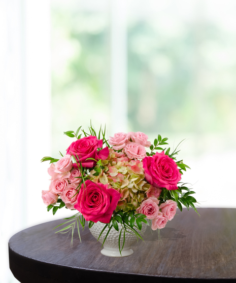 Tickled Pink everyday floral arrangement featuring hot pink roses, light pink spray roses, and lime-green hydrangeas in a white textured beaded pedestal vase.
