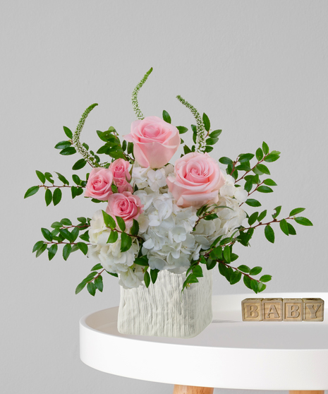 It’s a Girl flower arrangement with pink roses, white hydrangeas, and snapdragons in an ivory cube vase