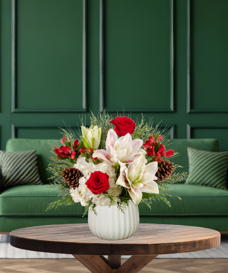 Jolly Jingle Berry Christmas arrangement with white lilies, red roses, white hydrangeas, red alstroemeria, red berries, pine cones, and evergreen in a textured white vase