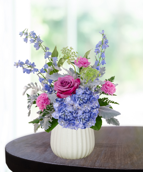 Sweet June flower arrangement in a white vase featuring pink roses, blue hydrangeas, lavender liatris, and delphinium