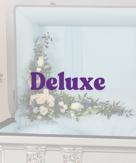 A Touch of Color casket lid floral piece with white roses, blue delphinium, and greenery in a casket corner