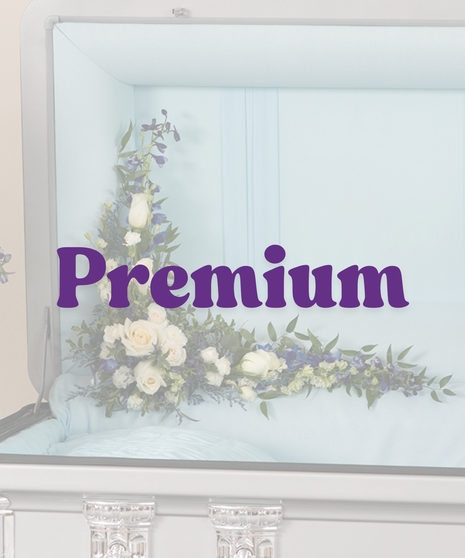A Touch of Color casket lid floral piece with white roses, blue delphinium, and greenery in a casket corner