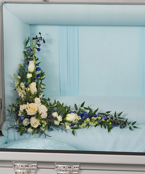 A Touch of Color casket lid floral piece with white roses, blue delphinium, and greenery in a casket corner