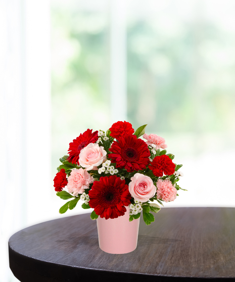 Love Bug Valentine's flower arrangement with red gerbera daisies, pink roses, red carnations, and white filler flowers in a matte pink vase.