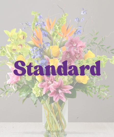 Maui Signature flower arrangement with birds of paradise, pink lilies, green orchids, yellow roses, and blue delphinium in tall glass vase