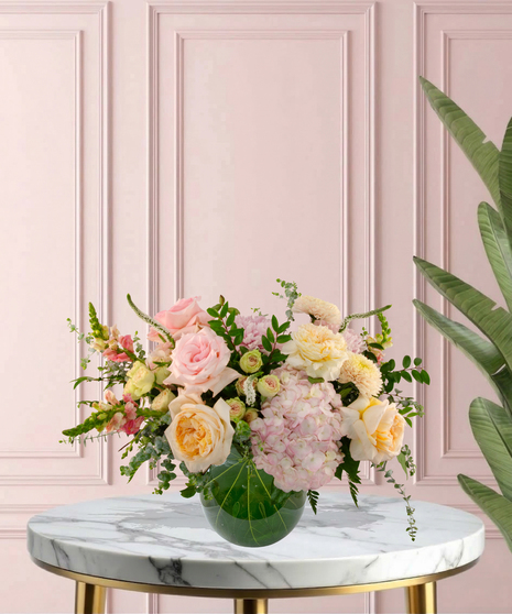 Momosa Signature flower arrangement featuring peach garden roses, pink hydrangeas, blush roses, and white veronica in an emerald-green glass bubble bowl.