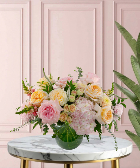 Momosa Signature flower arrangement featuring peach garden roses, pink hydrangeas, blush roses, and white veronica in an emerald-green glass bubble bowl.