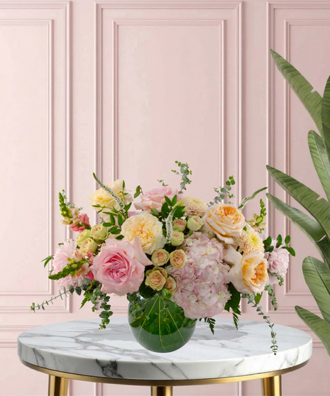 Momosa Signature flower arrangement featuring peach garden roses, pink hydrangeas, blush roses, and white veronica in an emerald-green glass bubble bowl.