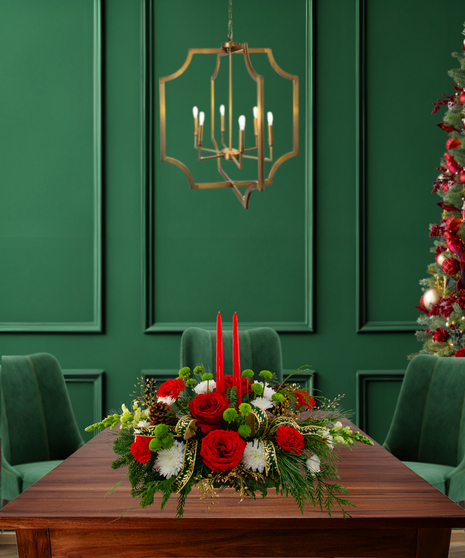 The More the Merrier centerpiece with red roses, carnations, hydrangeas, mums, pine cones, red berries, evergreen, and two red candles in a gold rectangular container