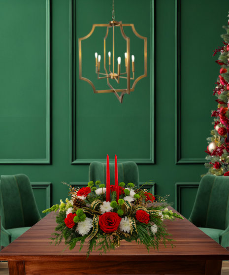 The More the Merrier centerpiece with red roses, carnations, hydrangeas, mums, pine cones, red berries, evergreen, and two red candles in a gold rectangular container