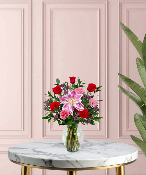 Open Arms Mother's Day flower arrangement featuring red roses, pink rose lilies, and more in a traditional glass vase.