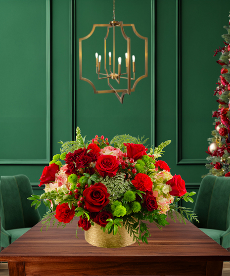 Noel classic Christmas flower arrangement with red roses, red carnations, green button mums, green hydrangeas, Bells of Ireland, and evergreen in a gold textured container