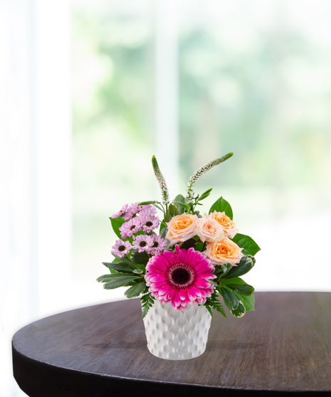 Radiant Energy floral arrangement with hot pink gerbera daisy, orange tulips, peach spray roses, and white veronica in a white textured honeycomb vase.