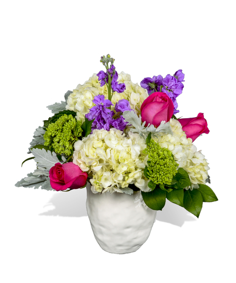 A white ceramic vase with white hydrangea, hot pink roses and purple stock.