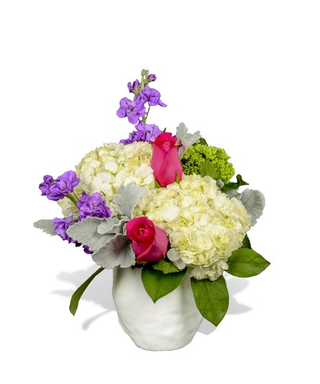 A white ceramic vase with white hydrangea, hot pink roses and purple stock.