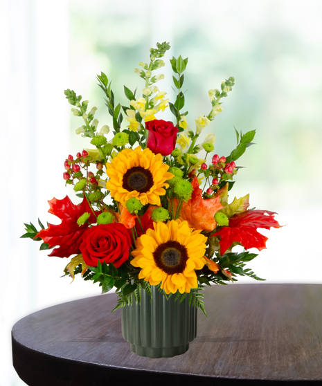 Orchard Sunset flower arrangement with sunflowers, red roses, yellow snapdragons, and autumn leaves in a green vase.