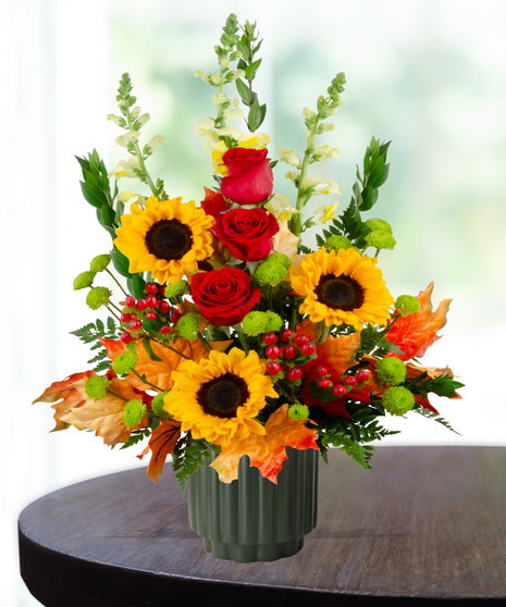 Orchard Sunset flower arrangement with sunflowers, red roses, yellow snapdragons, and autumn leaves in a green vase.