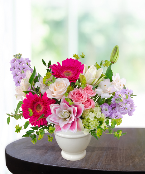 Pink Carats floral arrangement featuring pink roses, gerbera daisies, lilies, hydrangeas, and spring blooms in an ivory vase – an April birthday exclusive.