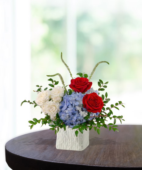 The Dynasty Bouquet exclusive Patriots flower arrangement with red roses, blue hydrangeas, garden roses, snapdragons, and veronica in a textured white vase for Super Bowl LX
